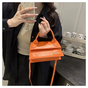 Détail d'un sac bandoulière en cuir orange vif avec logo doré et poignée courte chic