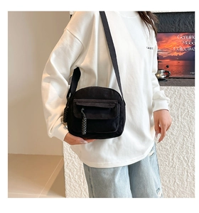 Detail of black corduroy crossbody bag featuring front pocket and woven zipper pull