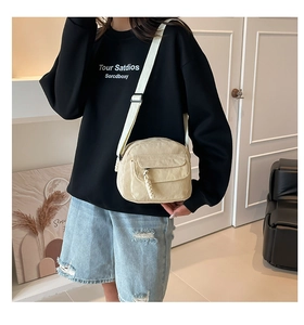 Detail of cream corduroy crossbody bag featuring a textured flap pocket and woven zipper