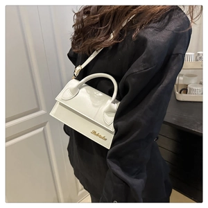 Detail van witte mini flap bag met goudkleurig logo en verstelbare schouderriem gedragen door model