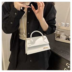 Detail van witte PU-lederen crossbodytas met elegant goudkleurig logo en handvat bovenaan