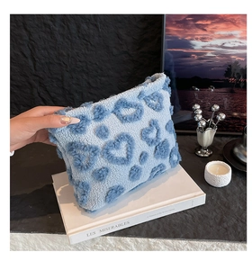 Dettaglio della pochette in velluto blu leopardato a cuore tenuta sopra un libro