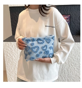 Detailed view of plush heart pattern blue cosmetic bag held by a model for travel storage