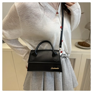 Detailopname van zwarte leren mini-crossbodytas met een goudkleurig cursief logo op de hoek