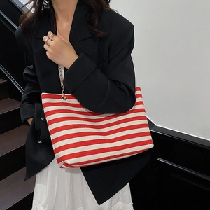 Red and white striped canvas tote bag with gold chain strap on shoulder of model
