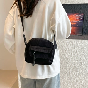 Sac à bandoulière carré en velours côtelé noir porté par un mannequin en style urbain