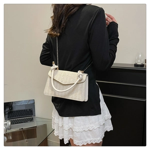 Détail d'un sac bandoulière tissé beige avec poignée anneau blanche et chaîne dorée
