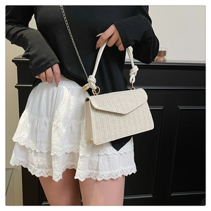 Détail d'un petit sac tissé crème avec chaîne dorée et poignée nouée blanche