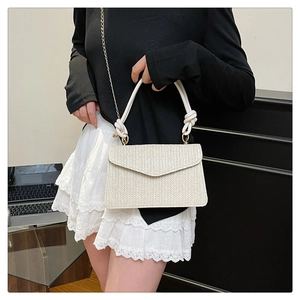 Détail du sac enveloppe tressé crème avec texture chevron et bandoulière dorée