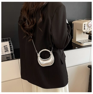 Mini bolso media luna plateado con asa circular y cadena en una escena de café