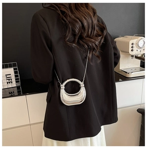 Detail of silver metallic crescent bag with round handle and thin chain strap on shoulder