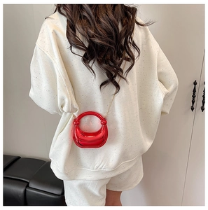 Detalle de un mini bolso rojo brillante con cadena dorada sobre una sudadera blanca