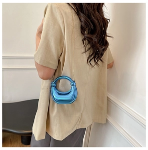 Bolso de mano azul metálico en forma de medialuna con cadena dorada sobre traje beige
