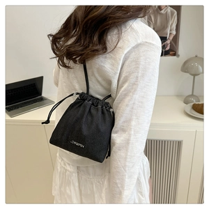 Dettaglio di una borsa a secchiello in denim nero con coulisse e logo JINGPIN in metallo