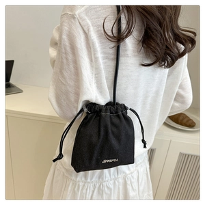 Détail du sac seau noir à cordon avec coutures blanches et logo porté par un mannequin