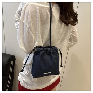 Detailed shot of dark blue denim bucket bag with drawstring closure and logo print