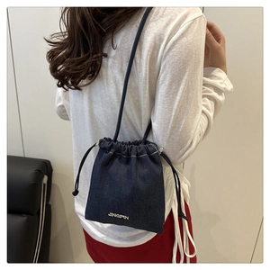 Dettaglio di una borsa a secchiello in denim blu scuro con coulisse e logo JINGPIN in metallo