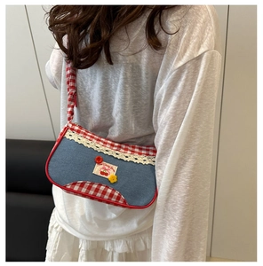 Detail of blue denim shoulder bag with red plaid trim and lace edges on a model
