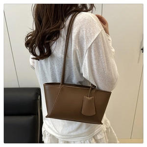 Minimalist dark brown leather tote bag worn by model on shoulder in a sleek indoor setting