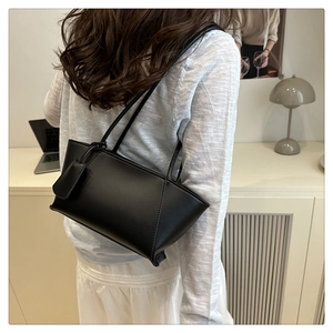 Gros plan d'un sac à main noir en cuir avec bandoulière porté par un mannequin en intérieur