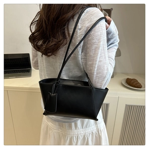 Side view of a black trapezoid tote bag worn on shoulder for minimalist style