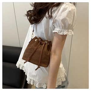 Close-up of brown suede drawstring bucket bag with gold metal eyelets and thin strap