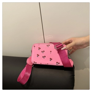 Close-up of pink camera bag with red cherry prints and a wide nylon shoulder strap