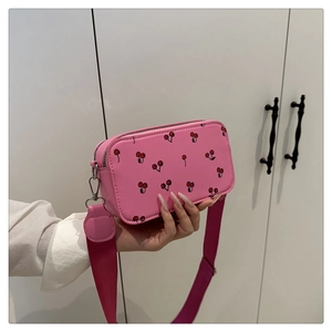 Detail view of pink crossbody bag with cherry prints and wide nylon shoulder strap