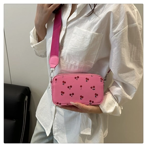 Detailed shot of pink cherry print crossbody camera bag with wide webbing shoulder strap