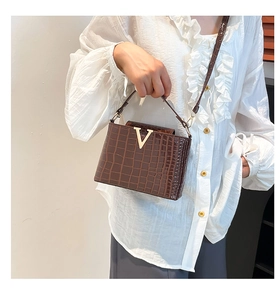 Detail of dark brown crocodile texture handbag with gold V metal buckle on white shirt