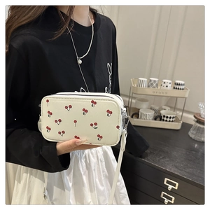 Detail of cute cherry print on white PU leather crossbody bag worn by a model