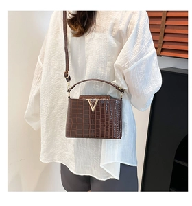 Close-up of brown crocodile texture handbag with a gold V-shaped buckle and crossbody strap