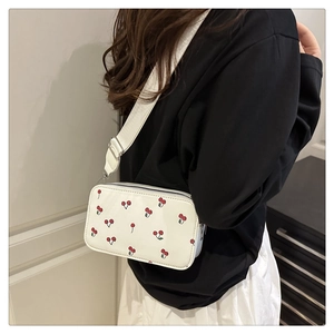 Close-up of white mini crossbody bag with cherry prints and wide fabric strap
