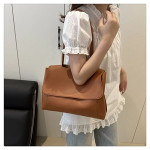 Brown faux leather tote bag worn as a shoulder bag by a model in a minimalist interior