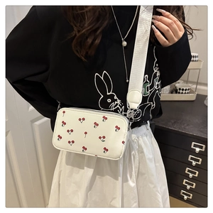 Detailed close-up of a white crossbody bag with red cherry prints and wide fabric strap