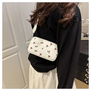 Detail view of mini white crossbody bag featuring red cherry prints and silver hardware