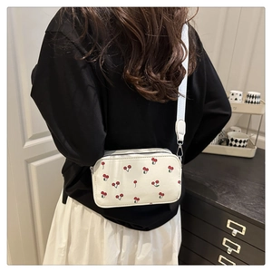 Detail of white camera bag with red cherry print and adjustable wide fabric strap