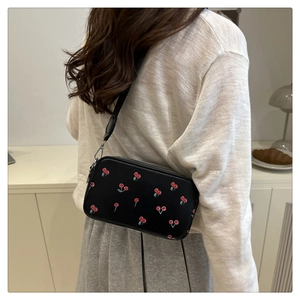Detailed view of black crossbody bag with cherry print worn by a model in a cozy room