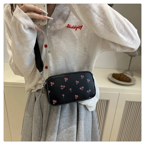 Detail of crossbody bag with cherry print and wide strap on model in bright setting