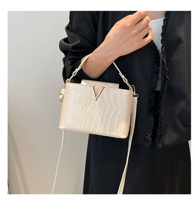 Detail of ivory faux-croc texture and golden V-shaped buckle on stylish handbag
