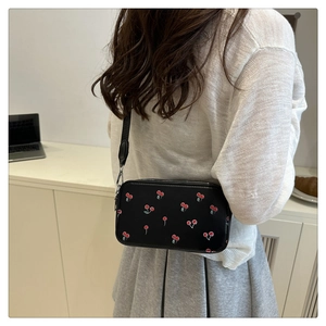 Detailed view of black crossbody bag with red cherry print and adjustable strap