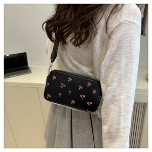 Detail of black crossbody bag featuring a cherry print and adjustable wide strap