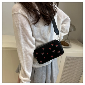 Detail of crossbody bag with cherry print, black leather texture and wide strap on a model
