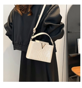 Detail view of cream stone-textured bucket bag with gold V-buckle and fine hardware