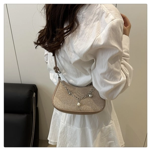 Detail of champagne gold hobo bag featuring metal chain with pearl and heart charms