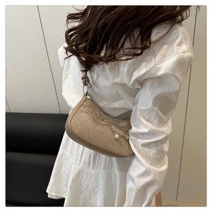 Close-up of champagne glossy underarm bag with decorative silver chain and pearl heart charms