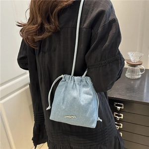 Fashionable blue denim bucket bag with drawstring closure worn as a crossbody bag