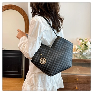 Détail du sac seau noir à imprimé lettres M avec breloque dorée et ouverture en V