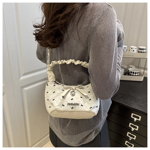 Close-up of cream quilted shoulder bag with black bows, ruffles, and heart pendant
