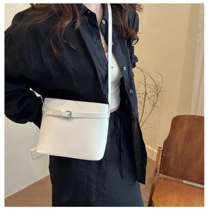 Détail d'un sac seau blanc à grain avec boucle argentée et bandoulière porté par un mannequin